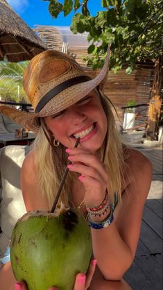 a woman wearing a straw hat holding a green coconut