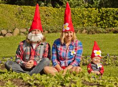 a man and woman sitting on the ground with two gnomes wearing red hats in front of them