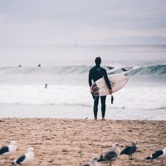 a man holding a surfboard on top of a sandy beach next to the ocean