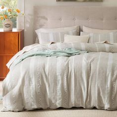 a bed with white sheets and pillows in a bedroom next to a nightstand filled with flowers