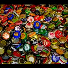 there are many different colored bottle caps on the table together and one is full of them