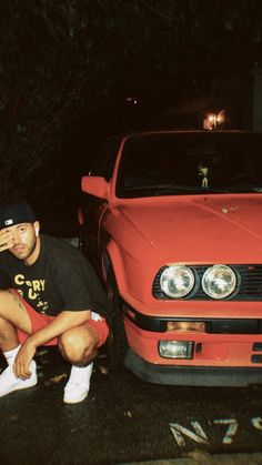 a man sitting on the ground next to a red car with his head in his hands