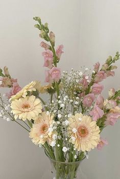 a glass vase filled with lots of flowers on top of a wooden table next to a white wall