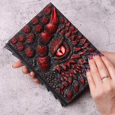 a woman's hand is holding an intricately designed book with red paint on it