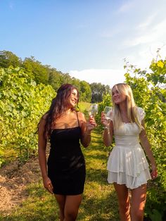 two beautiful women standing next to each other holding wine glasses in front of some vines