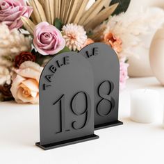 two black table numbers with flowers and candles in front of them on a white surface