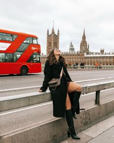 a woman sitting on a bench in front of a red bus and big ben, london