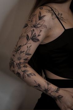 a woman's arm with flowers and leaves tattooed on her left arm, behind her is a black tank top