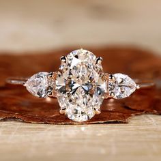 Close-up of an oval diamond ring in a rose gold setting Oval And Pear Engagement Ring, Oval With Side Stones, Oval Three Stone Engagement Ring, Three Stone Oval Engagement Ring, Three Stone Engagement Rings Oval, Fall Guy, Moissanite Vs Diamond, Oval Engagement Ring, Colored Diamond Rings