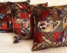 two decorative pillows sitting on top of a white bed covered in red and brown fabric