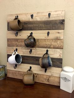 a wooden wall mounted with coffee mugs and cups on it's hooks, next to a canister