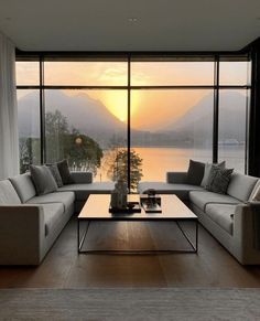 a living room filled with furniture and a large window overlooking the water at sunset or dawn