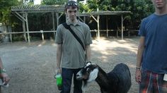 two men standing next to each other with a goat in the foreground and another man holding a beer