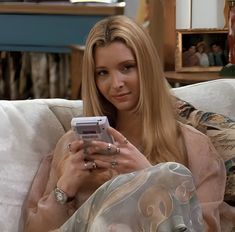 a woman sitting on a couch holding a cell phone in her hand and looking at the camera