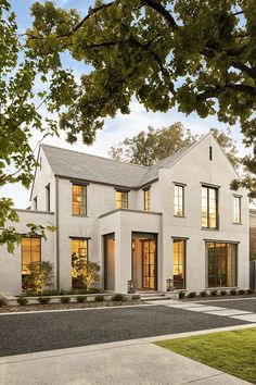 a large white house with lots of windows on it's sides and trees in the front yard