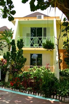 a yellow house with white balconies and green plants in the front yard area