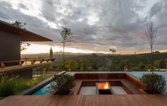 a fire pit in the middle of a wooden deck next to a swimming pool at sunset