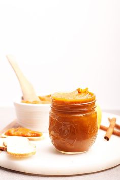 a jar of homemade maple pumpkin butter next to some cinnamon sticks and an apple slice