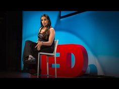 a woman sitting on top of a white chair in front of a blue wall with red letters