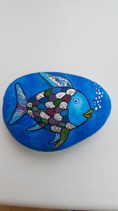 a painted rock sitting on top of a white table next to a blue object with an image of a fish