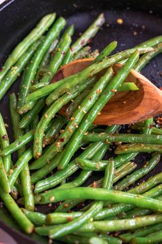 green beans being cooked in a skillet with wooden spoon and pepper flakes on the side