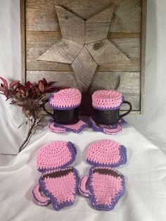 three crocheted mitts and two cups on a bed