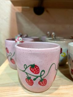 three cups sitting on top of a table next to each other with strawberries painted on them