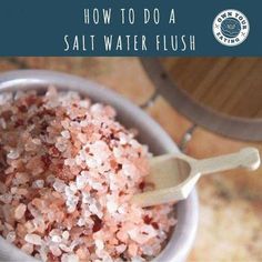 a white bowl filled with pink salt on top of a wooden table next to a spoon