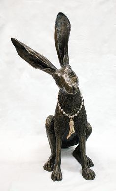 a statue of a rabbit wearing a bead around its neck sitting on a white surface