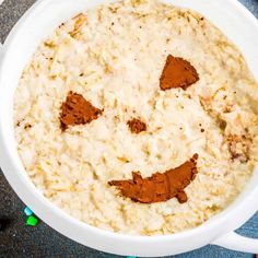 a white bowl filled with oatmeal topped with a face drawn on it