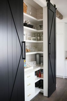 an open pantry door in a kitchen with white cupboards and black doors on both sides