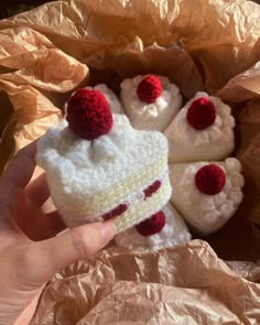 a hand holding a piece of crocheted cake with cherries on the top