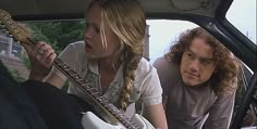 two people sitting in a car with guitars on the back seat and one person holding an electric guitar