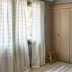 a room with a chair, closet and curtains on the windowsill in front of a window