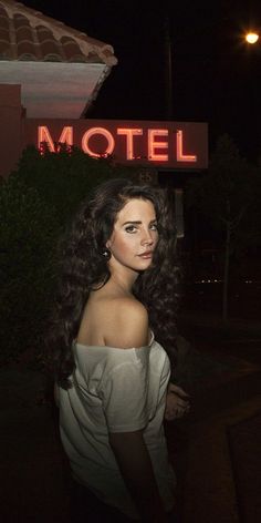 a woman standing in front of a motel sign at night with her hair blowing in the wind