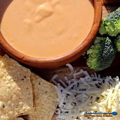 a wooden bowl filled with cheese and tortilla chips next to broccoli