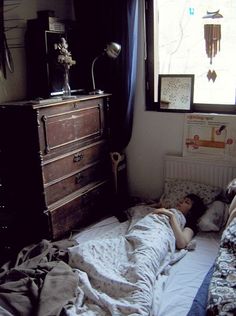 a person laying on a bed in a bedroom next to a dresser and window with curtains