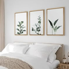 three framed pictures hang above a bed in a white bedroom with neutral linens and pillows