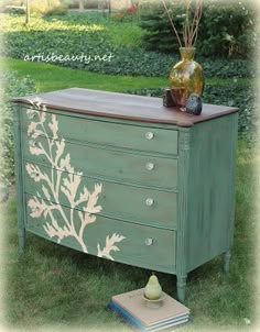 an old dresser painted in green and gold with flowers on the drawers is sitting outside