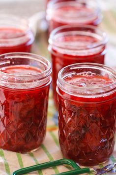 several jars filled with red liquid sitting on top of a green and white table cloth