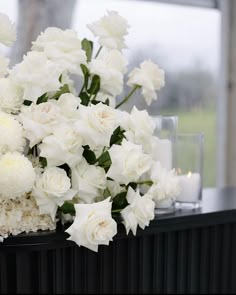 white flowers and greenery are arranged on a black table with candles in the background