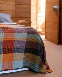 a bed with a plaid blanket on top of it in a bedroom next to wooden walls