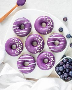 purple donuts with white frosting and blueberries on a plate next to spoons