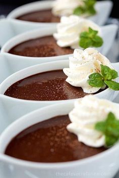 chocolate desserts with whipped cream and mint garnish in small white bowls on a table