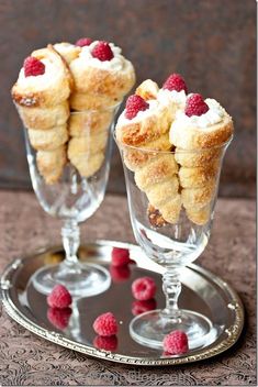 two small desserts are sitting on a silver tray with raspberries in them