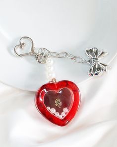 a red heart shaped keychain on a white cloth with two charms attached to it