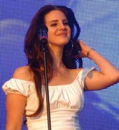 a woman standing in front of a microphone with her hand on her head and wearing a white dress