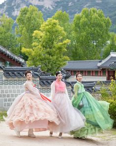 three women in long dresses are posing for the camera with mountains and trees in the background