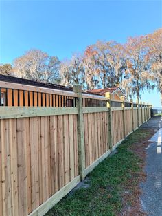 a wooden fence next to a road with trees in the background