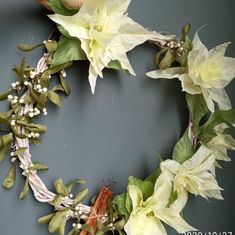 a wreath with white flowers and greenery is displayed on a gray background, close up